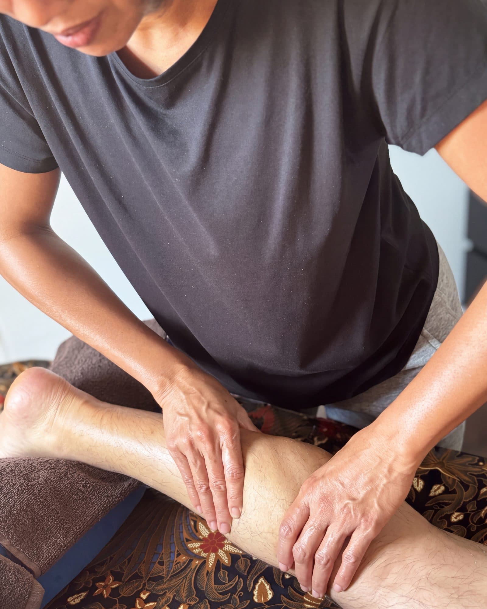 Les mains de Mini pendant un massage balinais, sur le batik de sa table de massage