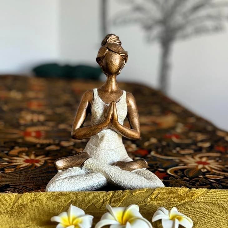 Statuette en prière posée sur le batik du salon, avec des fleurs de frangipanier
